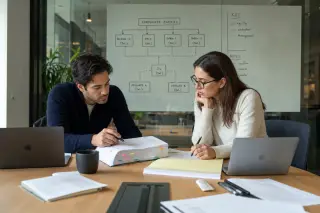 Lawyers in smart casual attire concentrate on an annotated report at a wooden meeting table, with a whiteboard and casual office elements in natural light.