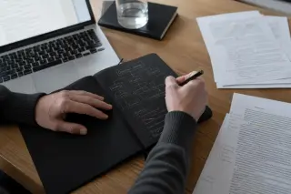 Close-up of a lawyer's hand annotating a legal memo on a wooden desk with documents, under soft natural light.