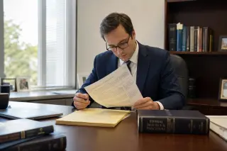 Lawyer alone at a wooden desk reading annotated documents in natural light, surrounded by legal books and notes, concentrated atmosphere.